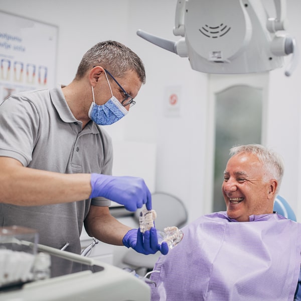 An elderly man sits in a dental chair and smiles